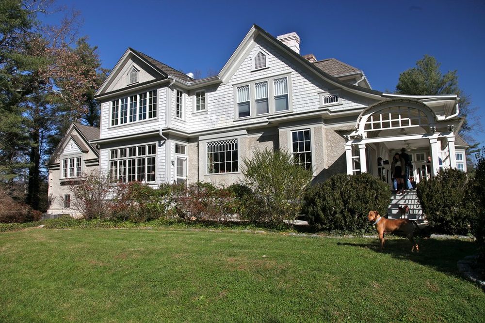 A large grey house with a gabled porch set behind a wide green lawn